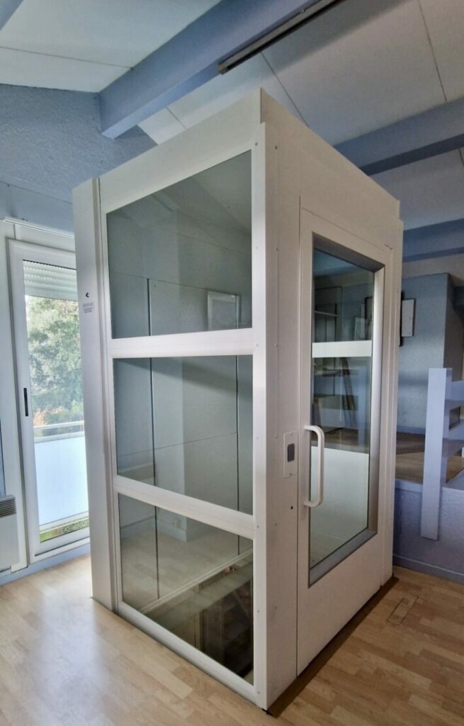 vue de l'ascenseur privatif vitré installé dans un intérieur lumineux, parquet clair, baie vitrée donnant sur l'extérieur en arrière-plan