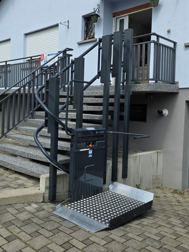 vue de face de la plateforme Lehner installée en bas des marches extérieures, plateau déroulé au niveau du sol, escalier en granit et garde-corps anthracite en arrière-plan