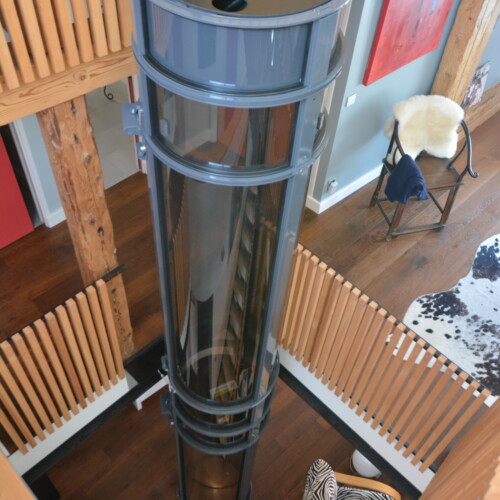 vue plongeante depuis la mezzanine sur l'ascenseur cylindrique transparent, bois naturel blond, parquet, garde-corps et œuvre d'art rouge en arrière-plan