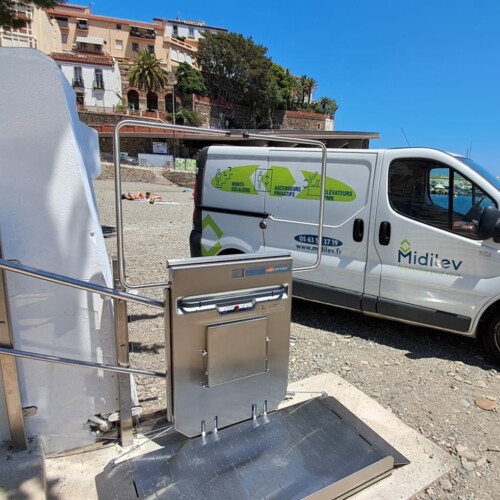 vue de la plateforme inox déployée au pied de l'escalier béton, vehicule Midilev garé sur les galets, port et Méditerranée en arrière-plan